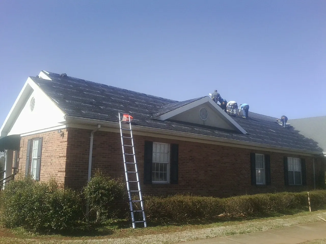 Crew tearing shingles off a brick ranch roof with a ladder set — Metal Roof Repair work by our crew in Pennington