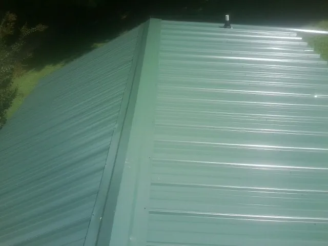 New green metal panels meeting at the ridge of a roof — Flat Roof Repair work by our crew in Pennington