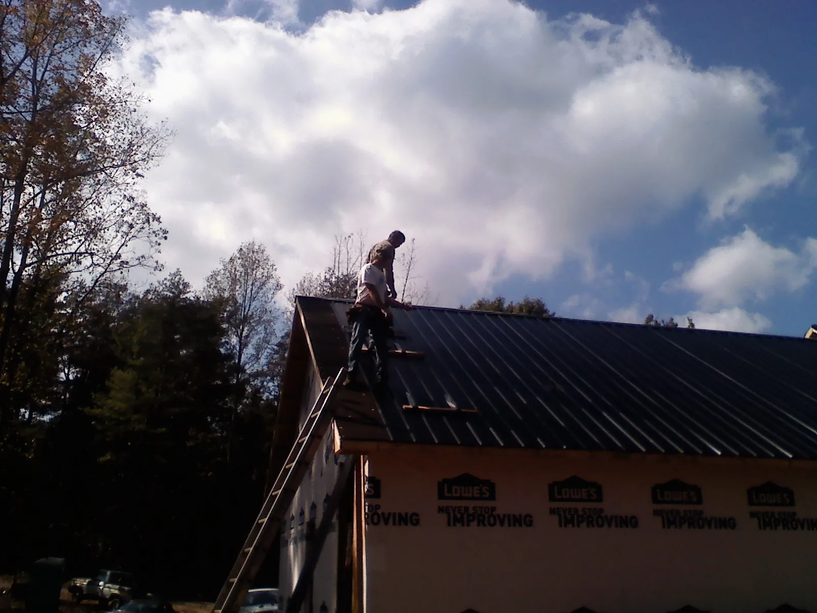 Roofer fastening dark metal panels high against a cloudy sky, from a Roof Inspection job in Pennington